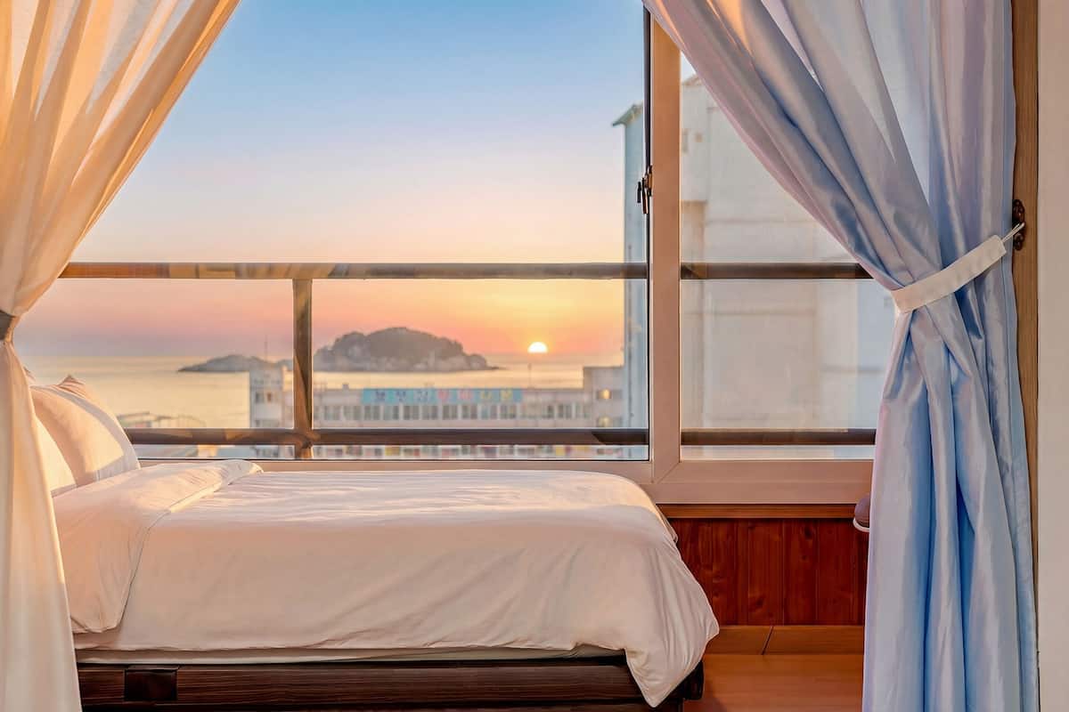 Une chambre avec une grande fenêtre, un lit et des rideaux.