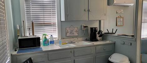 A compact kitchenette with a sink, a coffee maker, and a trash bin.