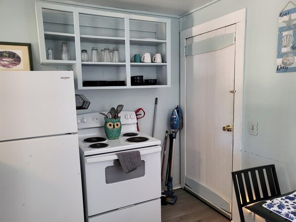 A compact kitchen with a white stove, a green owl-shaped pot holder, and a blue vacuum cleaner.
