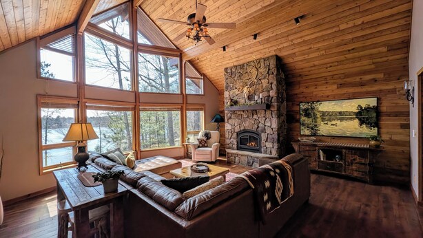 Un interior de cabaña acogedor con chimenea de piedra, ventanas amplias, una zona de estar confortable y un televisor.