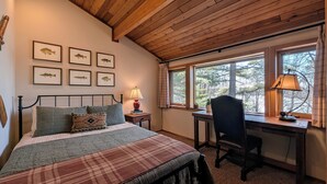 Un dormitorio con cama, escritorio y silla. En la pared, hay cuadros de peces enmarcados, una lámpara sobre el escritorio y una ventana con vistas a árboles.