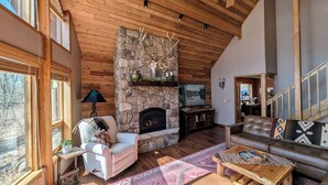 Una sala de estar acogedora con chimenea de piedra, techo de madera y vistas al exterior.