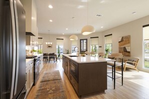 Una cocina moderna con una isla central, iluminación colgante y un área de comedor con sillas.