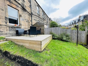 Un patio trasero con terraza de madera, mobiliario exterior y un edificio de piedra.