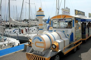 A miniature train with 'LE PETIT TRAIN' and 'DECTA FM' signage, parked in a marina with boats in the background. - Bright and cozy 2-room apartment close to the beach and shops, parking (LE GRAU DU ROI)