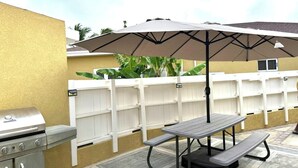Patio esterno con griglia, tavolo da picnic e ombrellone.