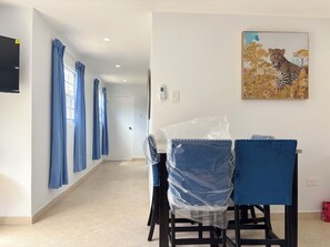 A hotel room with a dining area featuring blue chairs and a table, a painting of a leopard, and a tiled floor. - Primavera Vacation Home l close to beaches & airport (Oranjestad)