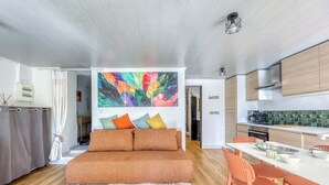 Ein modernes Wohnzimmer mit einer Couch, einem Essbereich mit Stühlen und einer Küche mit Holdekor und einem farbenfrohen, abstrakten Gemälde.