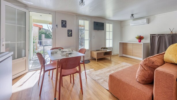 Ein modernes Wohnzimmer mit einer Couch, einem Esstisch mit Stühlen und einem an der Wand montierten Fernseher.