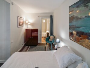 Ein Hotelzimmer mit Bett, Schreibtisch, Stuhl, einem Gemälde und einem durchgegangenen Tür sichtbaren Badezimmer.