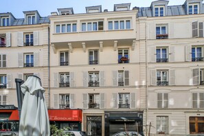 Ein mehrstöckiges Gebäude mit einer Reihe von Balkonen, einem Café mit roter Markise und einem Schönheitssalon.