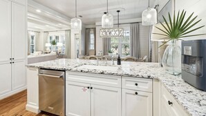Une cuisine moderne avec des meubles blancs, des plans de travail en granit et des luminaires suspendus.
