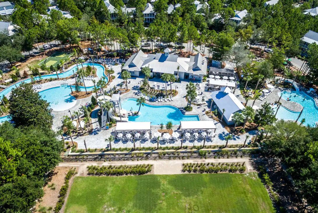 An aerial view of a resort with multiple swimming pools, lounge areas, and a golf course.