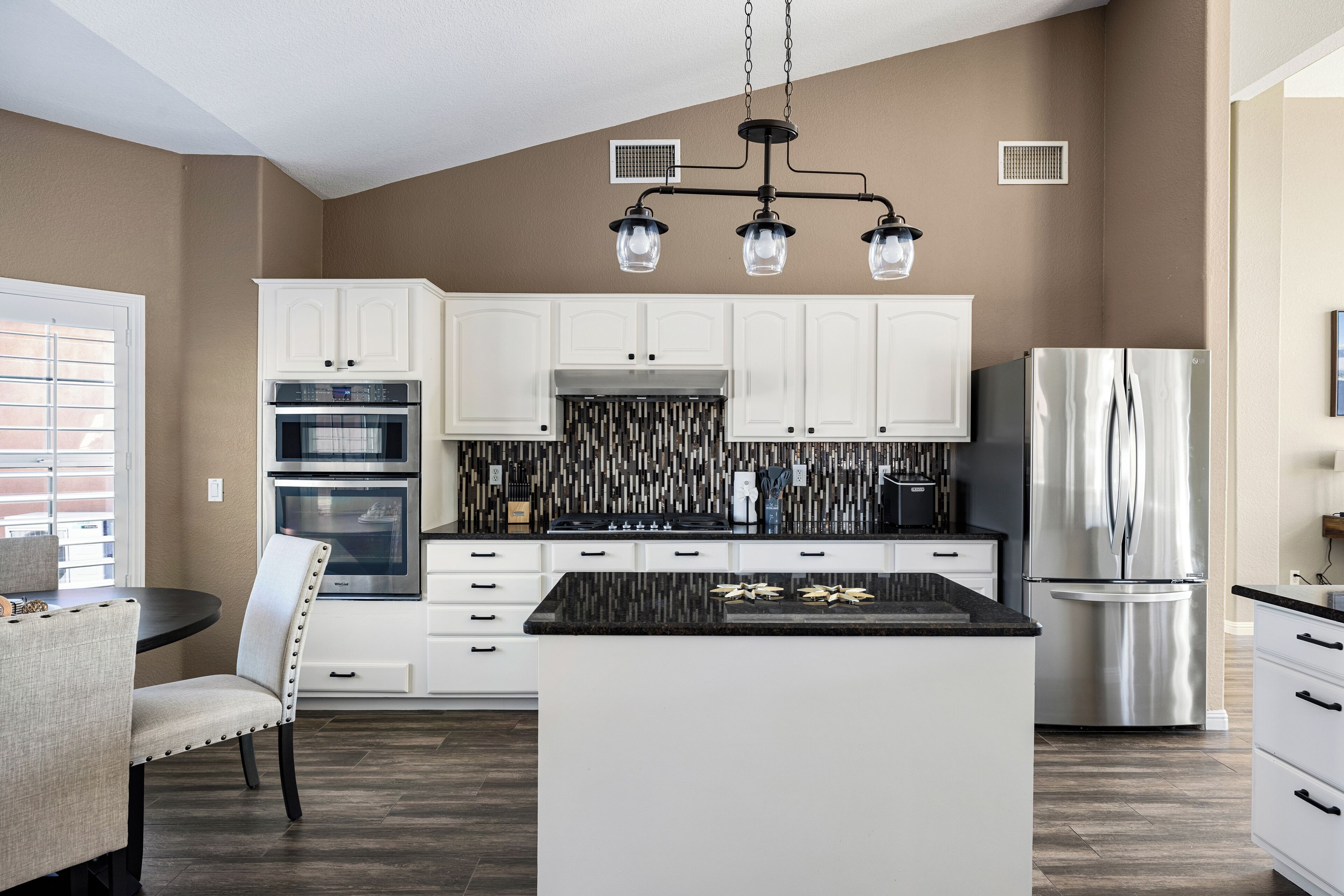 A modern kitchen with white cabinets, a central island, stainless steel appliances, and a patterned backsplash.
