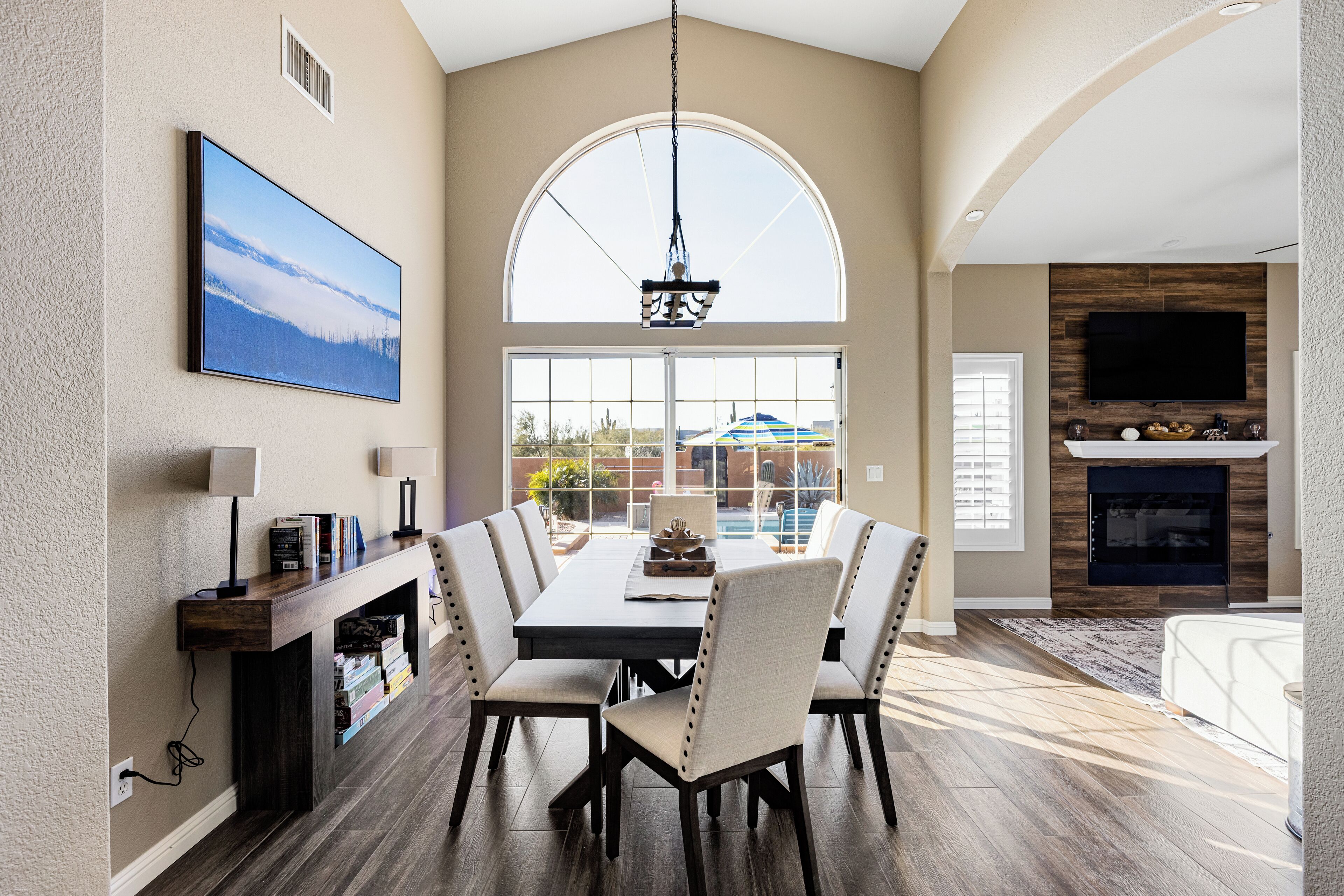 A dining area with a large table, chairs, and a hanging light fixture.