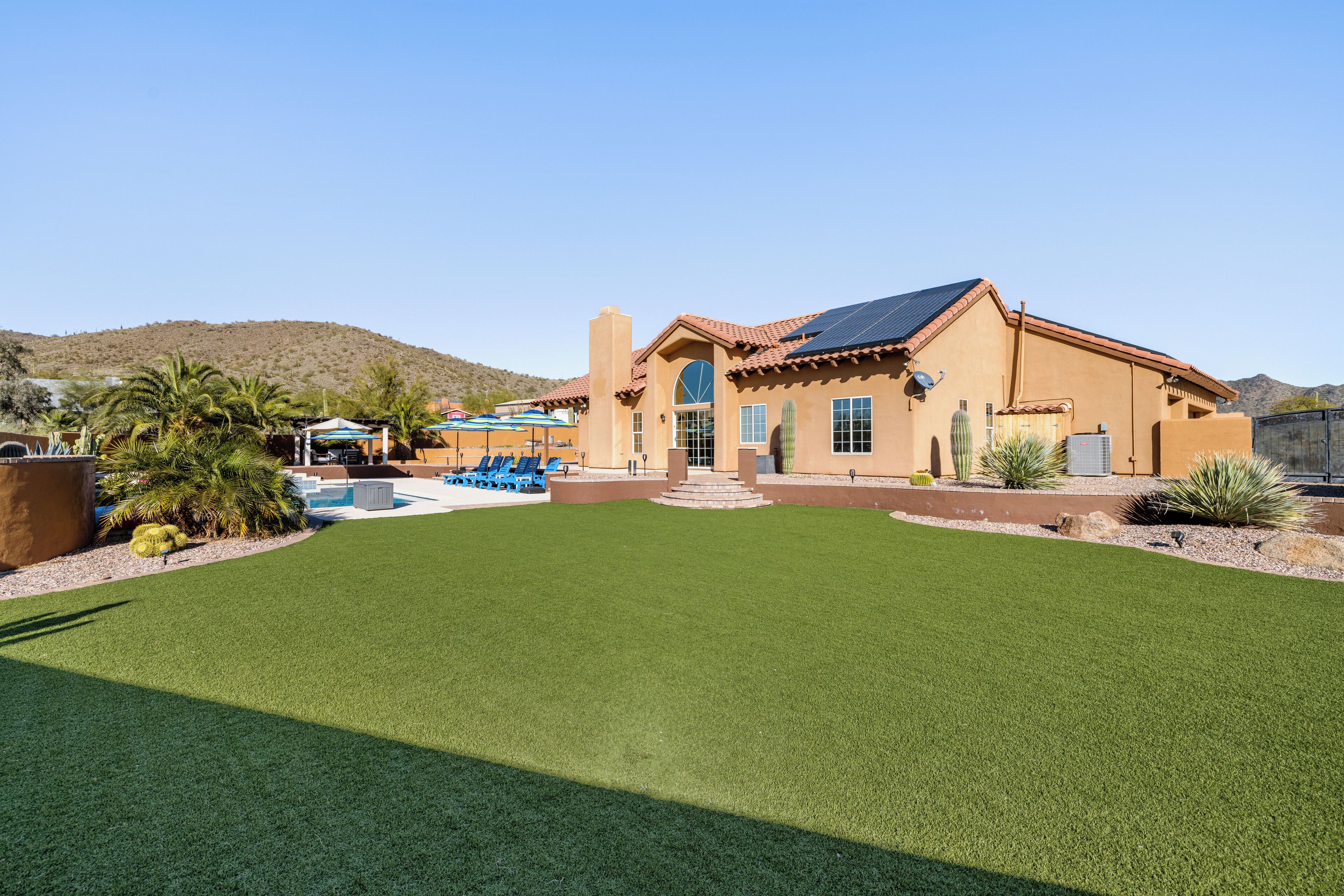 A house with a large lawn, a pool, and a desert landscape in the background.