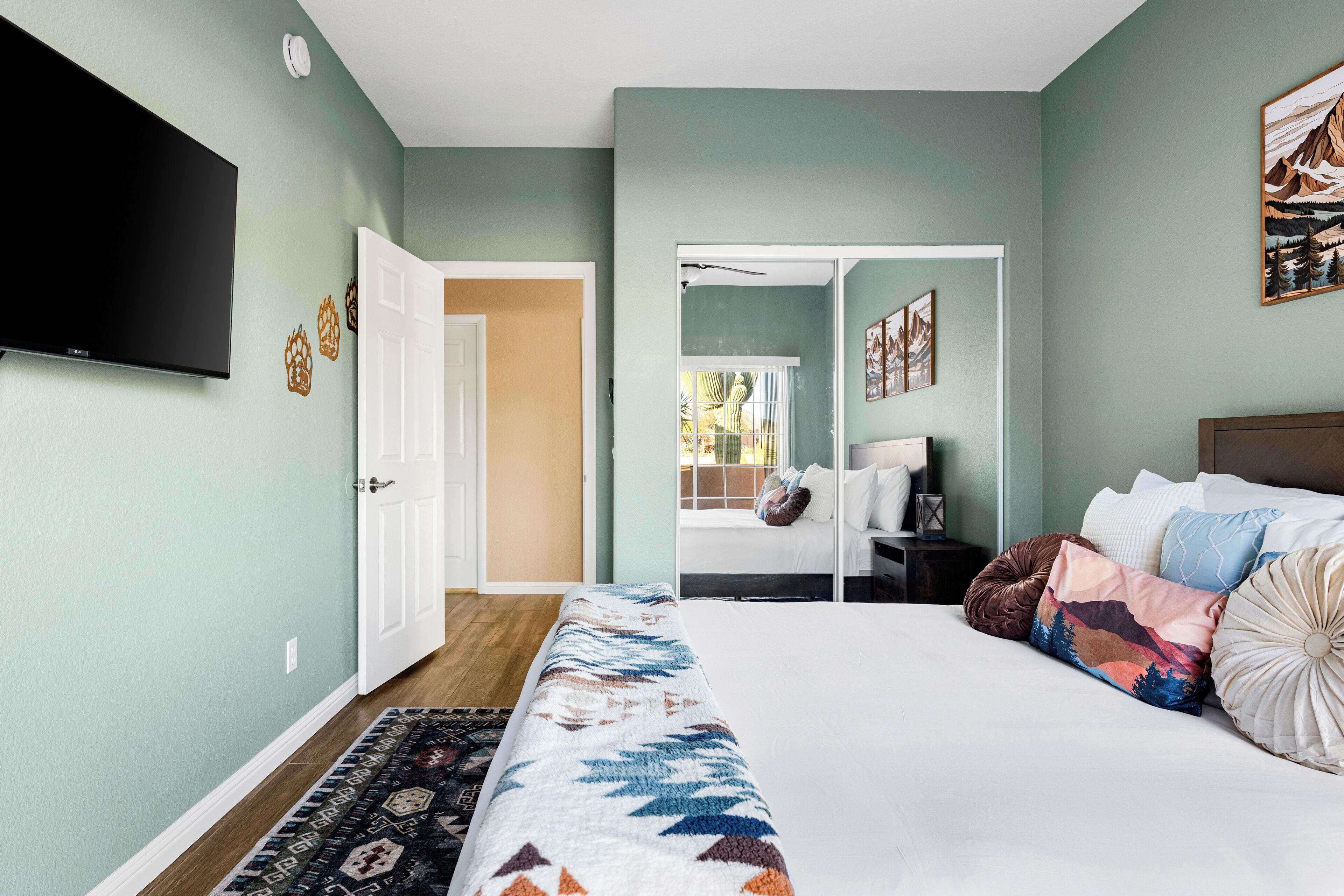 Quarto com cama, televisão na parede, porta para outro espaço e janela com vista.