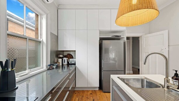 Une cuisine moderne avec des armoires blanches, un réfrigérateur en acier inoxydable et un plancher en bois.
