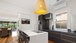 Une cuisine moderne dotée d’un grand îlot central, de meubles de rangement aux couleurs sombres et d’un luminaire suspendu.