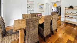 Un coin repas avec une table en bois et des chaises en osier, des murs blancs et un plancher en bois.