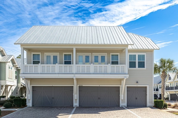 A two-story house with a balcony, three garage doors, and a clear blue sky. - Power & wifi on - 3 BR, close to the resort style pool, Big Chill & Bikes (Santa Rosa Beach)