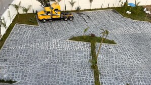 Un espace de stationnement où se trouve un camion jaune et où le sol présente un motif de pierres particulier.