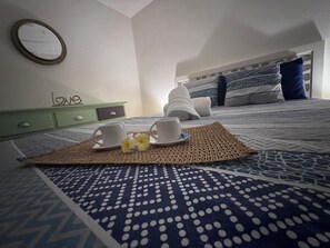 A neatly made bed with patterned bedding, a bedside table with a cup and saucer, and a green nightstand with a drawer. - Cosy little nest 2 min from Grand Case airport and 5 min from the beaches (Grand case)