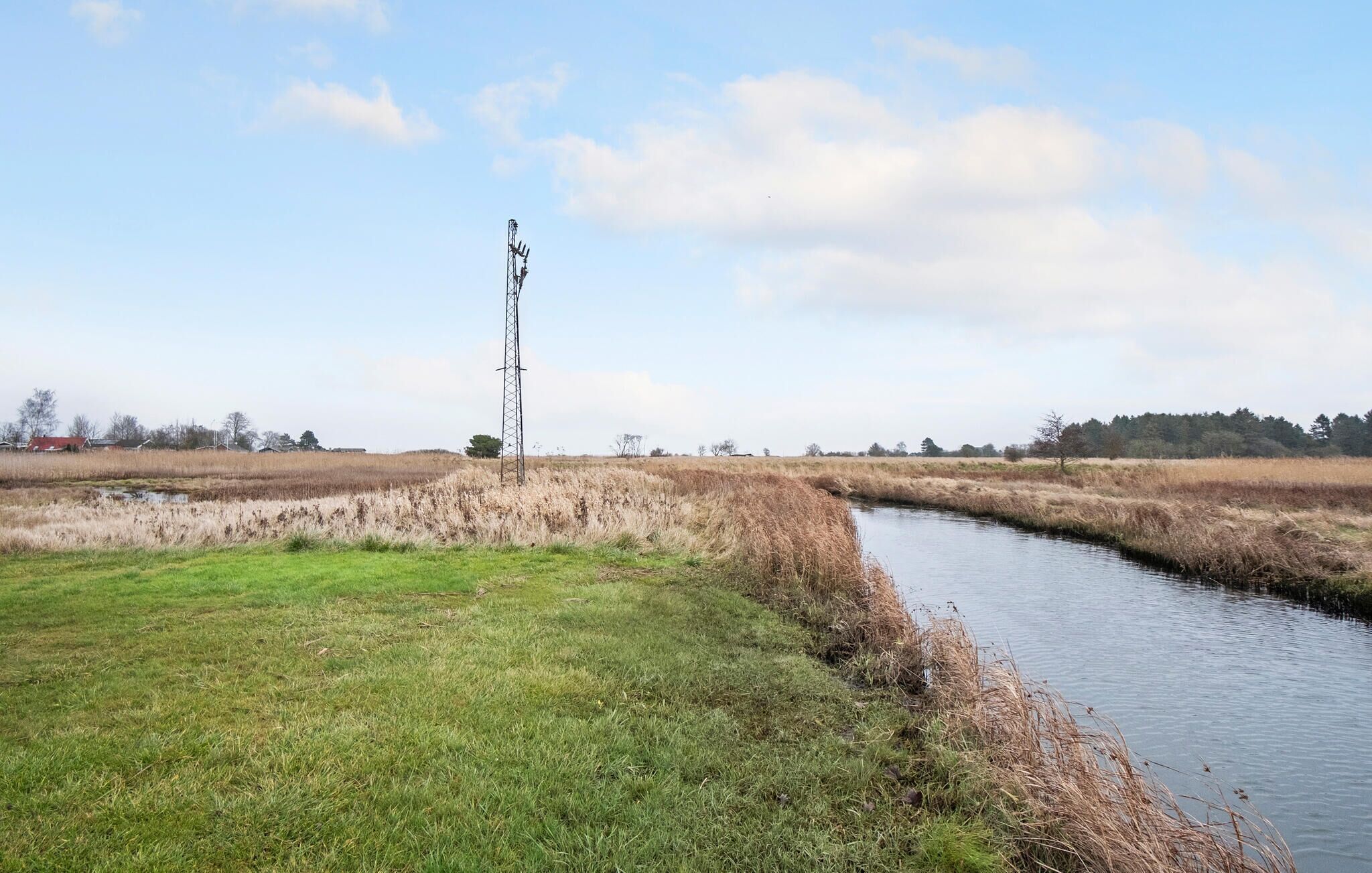 Een landelijk landschap met een waterloop, grasvelden en een hoge zendmast.