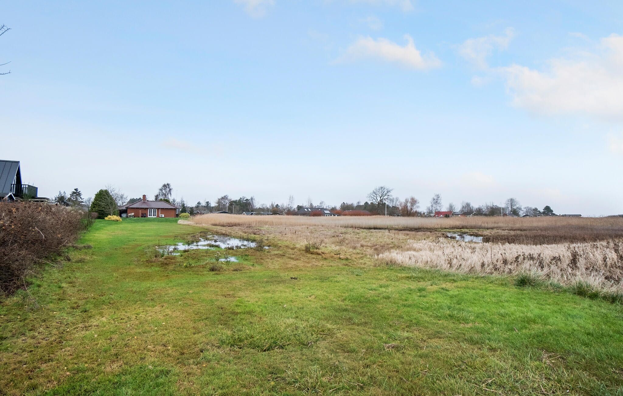 A rural landscape with a grassy field, a small pond, and a red house in the background.