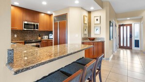 Una cocina moderna con encimeras de granito, electrodomésticos de acero inoxidable, armarios de madera y una zona de bar con sillas acolchadas.