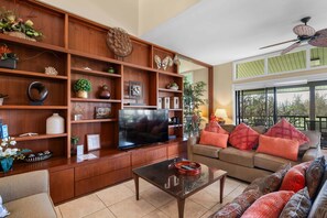 Ein Wohnzimmer mit Fernseher, Holzregalen, einer Couch und einem Deckenventilator.