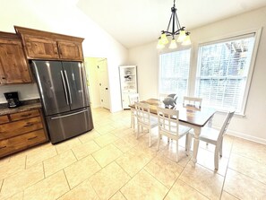 A kitchen with wooden cabinets, a stainless steel refrigerator, a dining table with chairs, and a chandelier. - Coastal Escape Includes Golf Cart, Bikes and Multiple Covered Outdoor Areas (Dauphin Island)