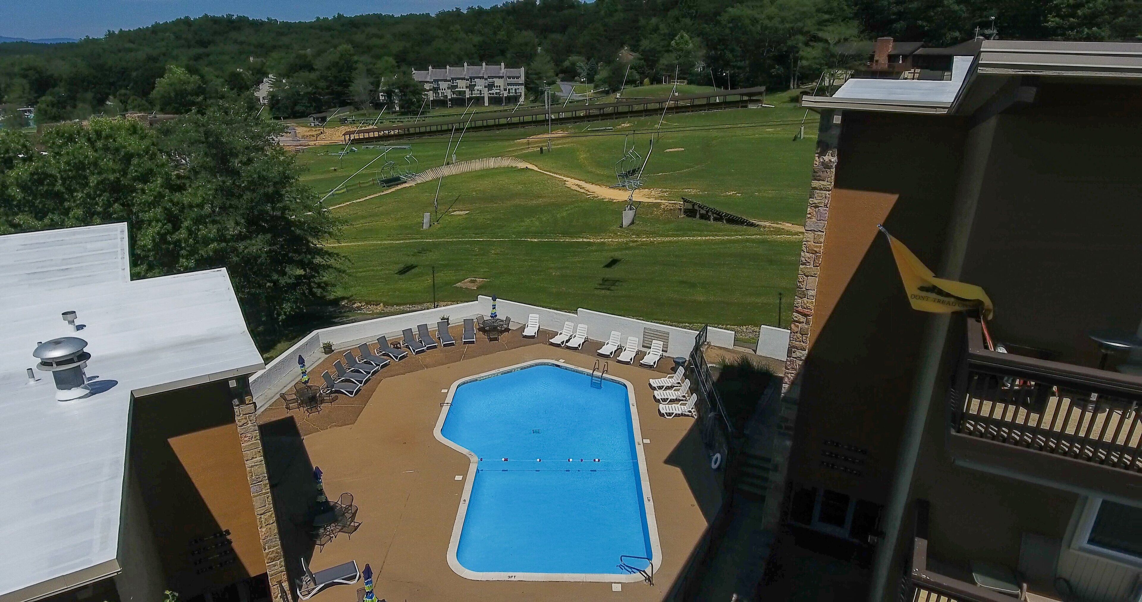 A swimming pool with lounge chairs, a tennis court, and a building in the background.