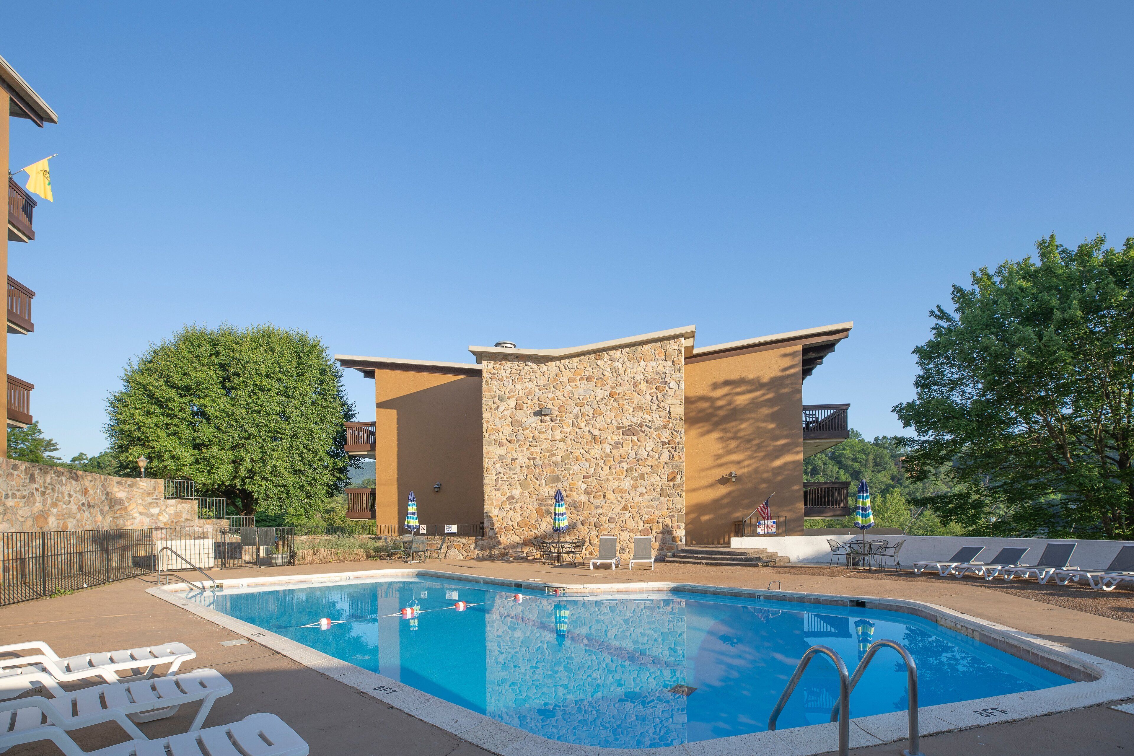 A swimming pool with lounge chairs and umbrellas, surrounded by stone walls and a clear blue sky.