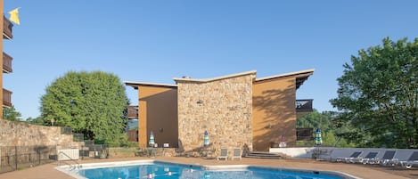 A swimming pool with lounge chairs and umbrellas, surrounded by stone walls and a clear blue sky.