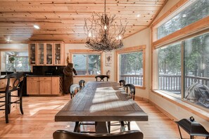 A spacious dining area with a large wooden table and chairs, a rustic chandelier, and large windows offering views of the outdoors. - Kindred Pines at Tahoe Donner by Tahoe Getaways - 3BR with Pool Table & HOA (Truckee)