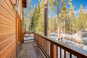 A wooden deck with a railing, overlooking a snowy forest with tall pine trees. - Kindred Pines at Tahoe Donner by Tahoe Getaways - 3BR with Pool Table & HOA (Truckee)