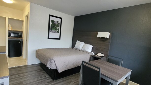 A hotel room with a bed, bedside table, chair, desk, and a small kitchenette. - Budget Inn (Durham)