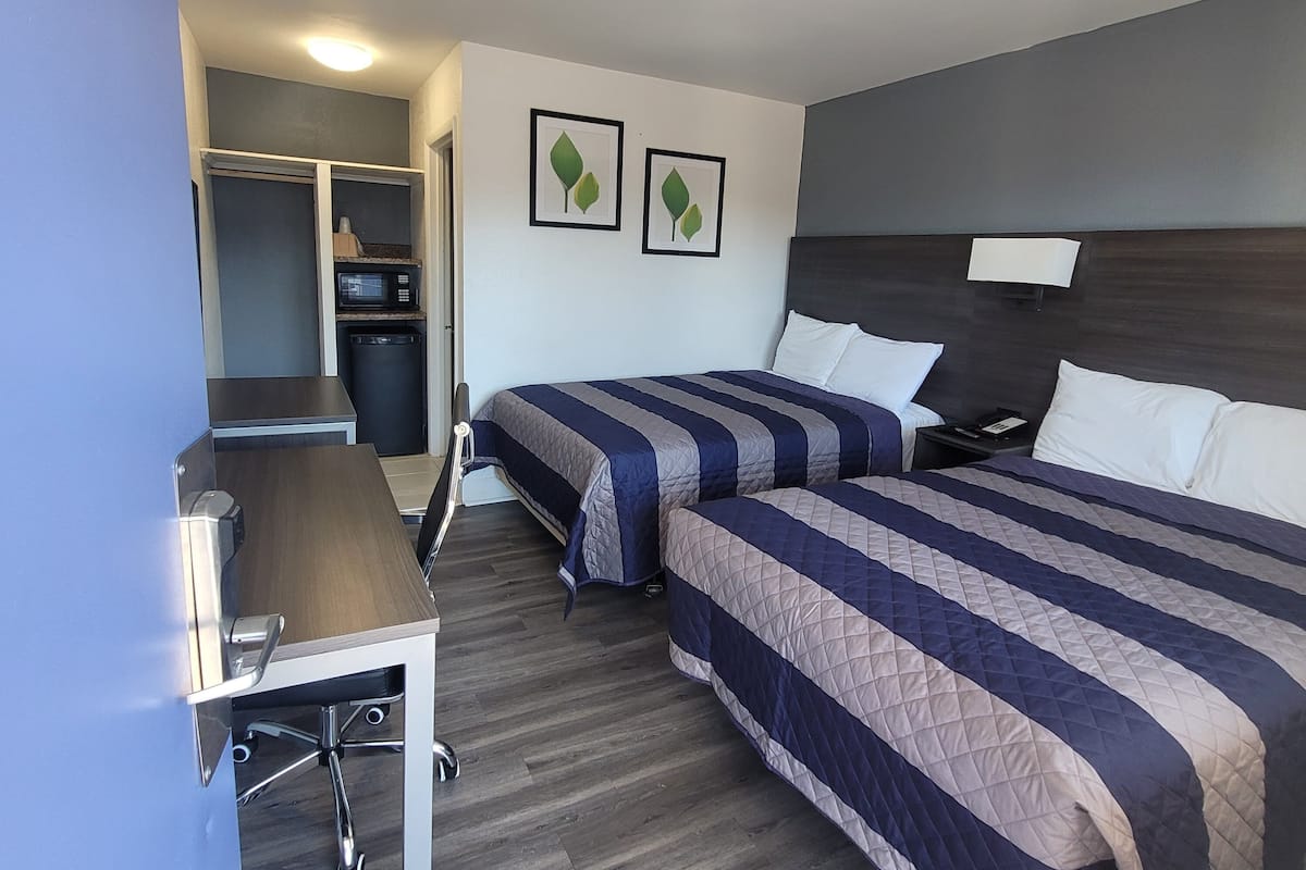 Habitación de hotel con dos camas, un escritorio, un microondas y un armario pequeño.