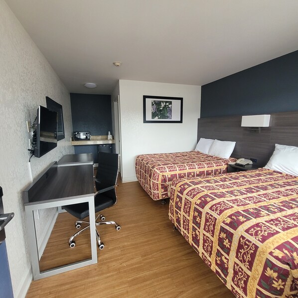 A hotel room with a desk, two beds, a television, a microwave, and a framed picture on the wall. - Budget Inn (Durham)