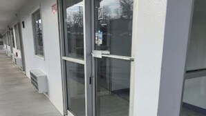 A row of hotel rooms with large sliding glass doors, a concrete walkway, and a white exterior wall. - Budget Inn (Durham)