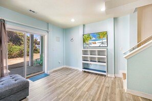 A living room with a sliding glass door, a flat-screen TV, and a staircase. - Sea Turtle Escape | Pool & Tennis Coastal Getaway (Kill Devil Hills)
