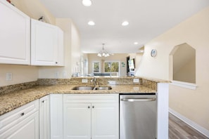 A kitchen with white cabinets, granite countertops, stainless steel appliances, and recessed ceiling lights. - Sea Turtle Escape | Pool & Tennis Coastal Getaway (Kill Devil Hills)