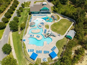 An aerial view of a resort with a large swimming pool, multiple sun loungers, and a building with a green roof. - Sea Turtle Escape | Pool & Tennis Coastal Getaway (Kill Devil Hills)