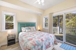Une chambre à coucher comprenant un lit, une table de chevet, un ventilateur de plafond et une vue sur l’extérieur grâce à de grandes fenêtres.