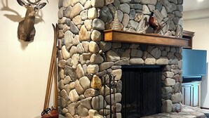 A stone fireplace with a mounted deer head and antlers, a wooden shelf with decorative items, and a pair of skis leaning against the wall. - Mountain Side luxury Condo (Ketchum)