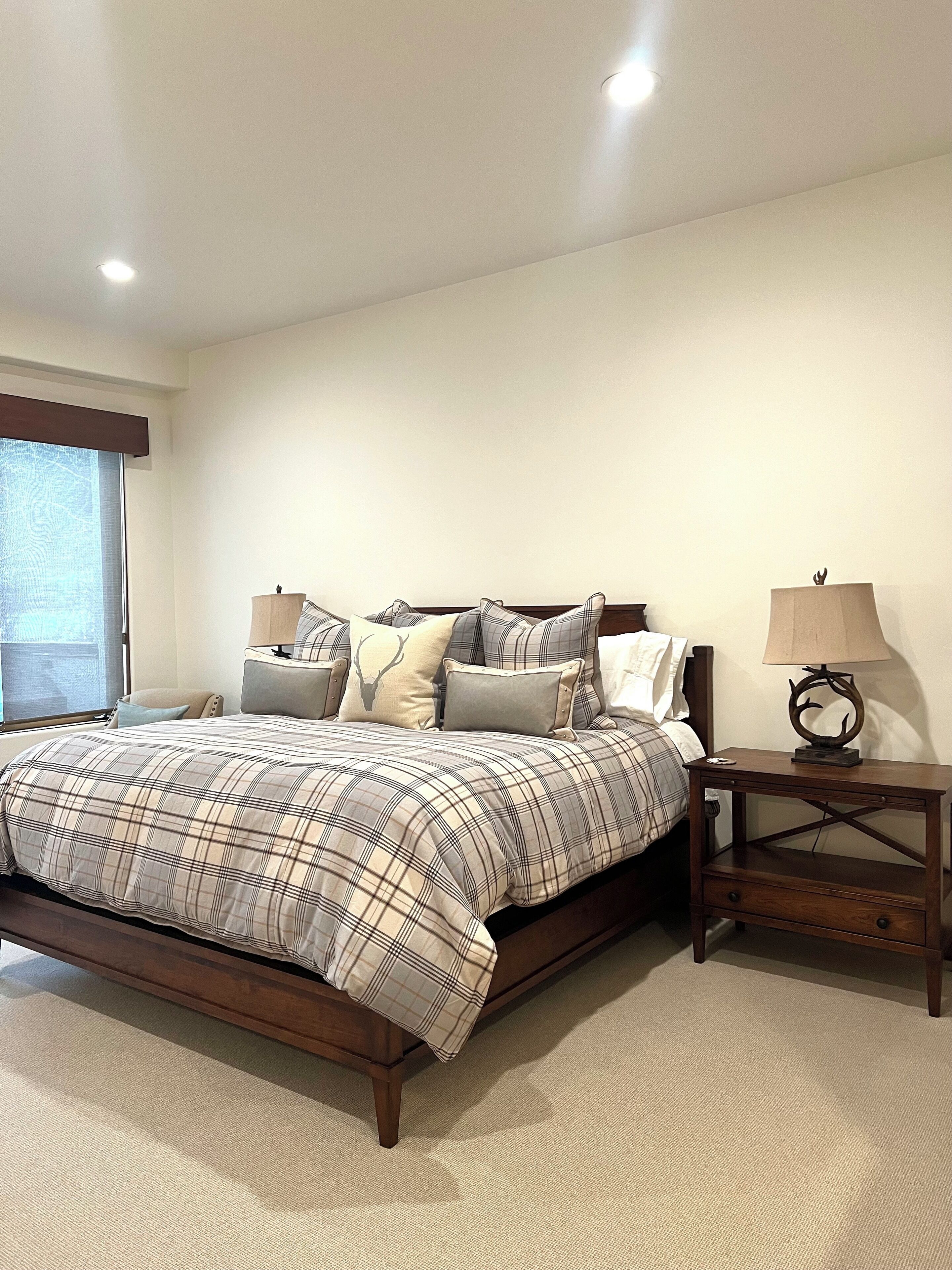 A bedroom with a bed, a nightstand, a lamp, and a window with blinds.