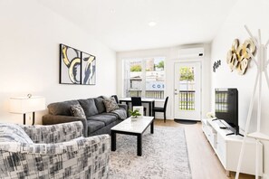 A modern living room with a sofa, a patterned armchair, a coffee table, and a TV. - Downtown Escape by Bathhouse Row & Convention Cntr (Hot Springs)