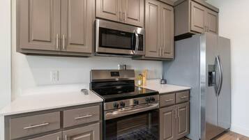 A modern kitchen with stainless steel appliances, beige cabinetry, and a white countertop.