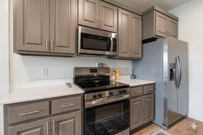 A kitchen with stainless steel appliances, beige cabinetry, and a white countertop. - Modern City Retreat- Walk to Convention Center (Hot Springs)